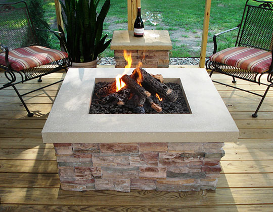 square fire pit with fire burning in it. Two chairs and table