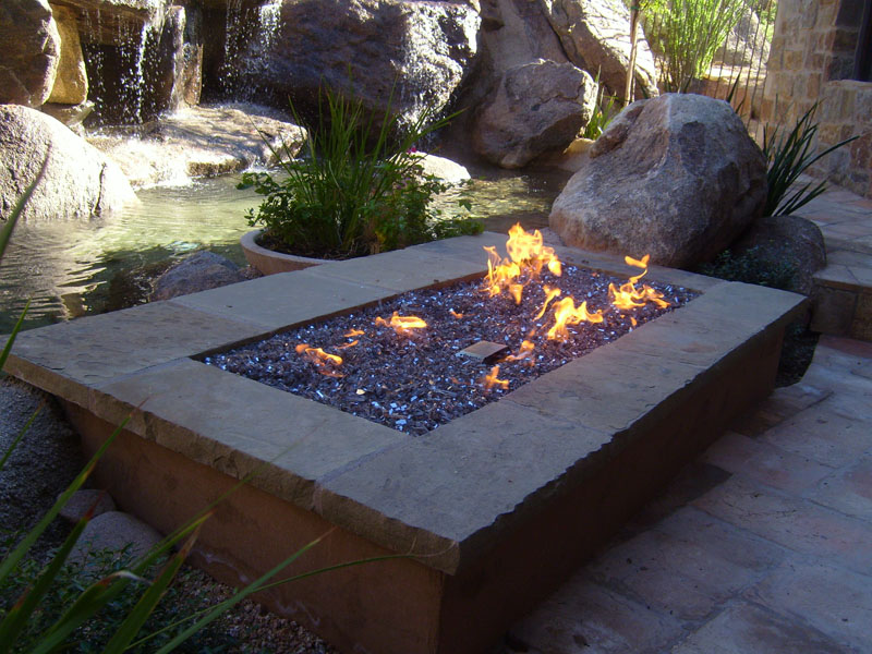 large rectangular firepit with fire burning and rocks in background