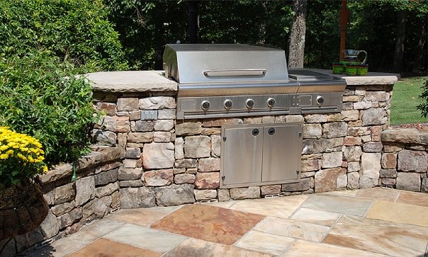 Santa Fe island style out door kitchen grill in rock outdoor kitchen with green bushes around it