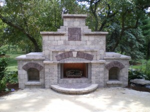 large grey outdoor fireplace with three fireboxes and large trees behind it 