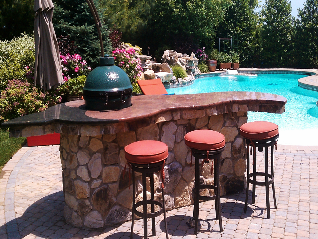 outdoor island with green egg and three bar stools next to pool on suny day